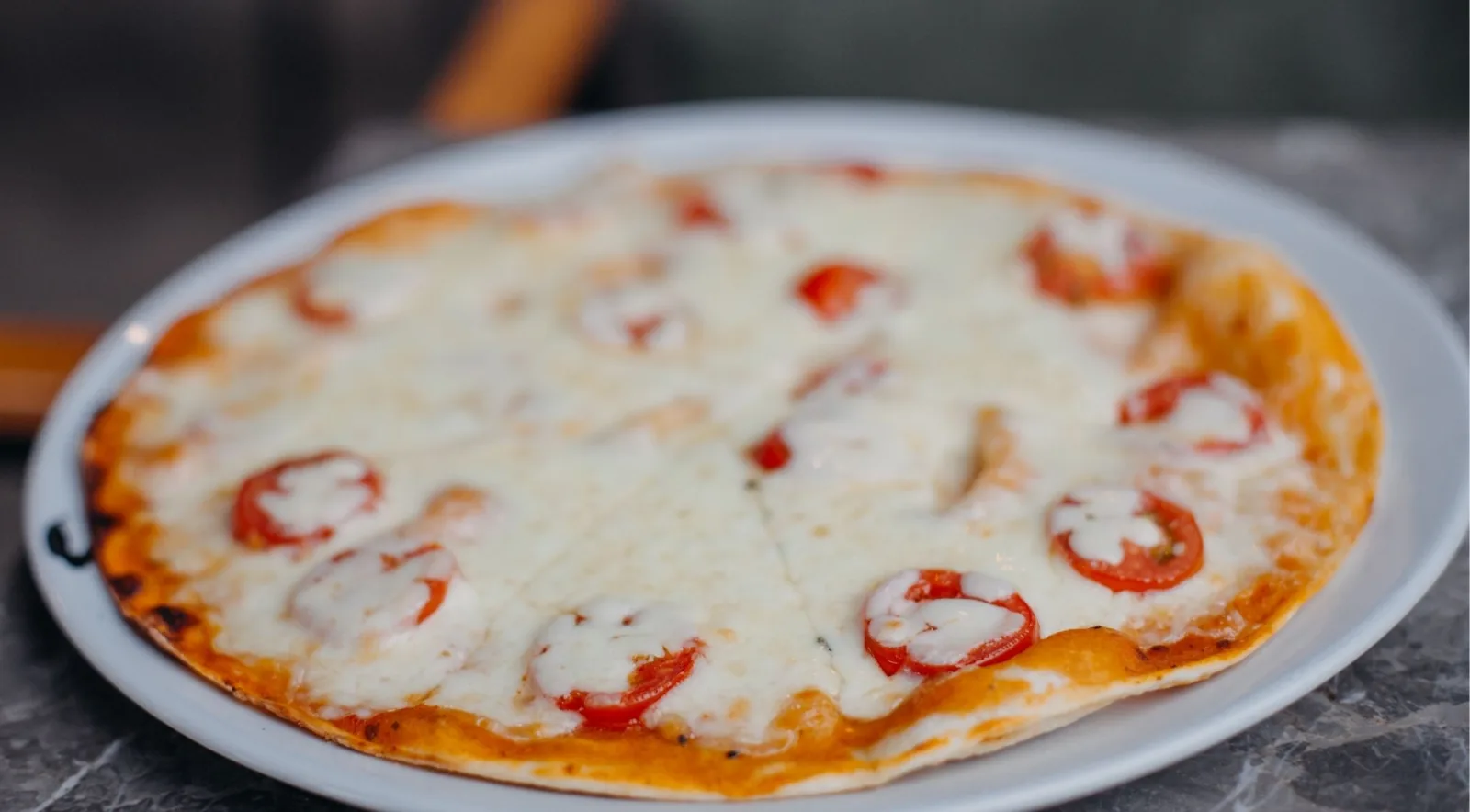 A Neapolitan Margherita pizza with melted mozzarella and cherry tomatoes served on a white plate