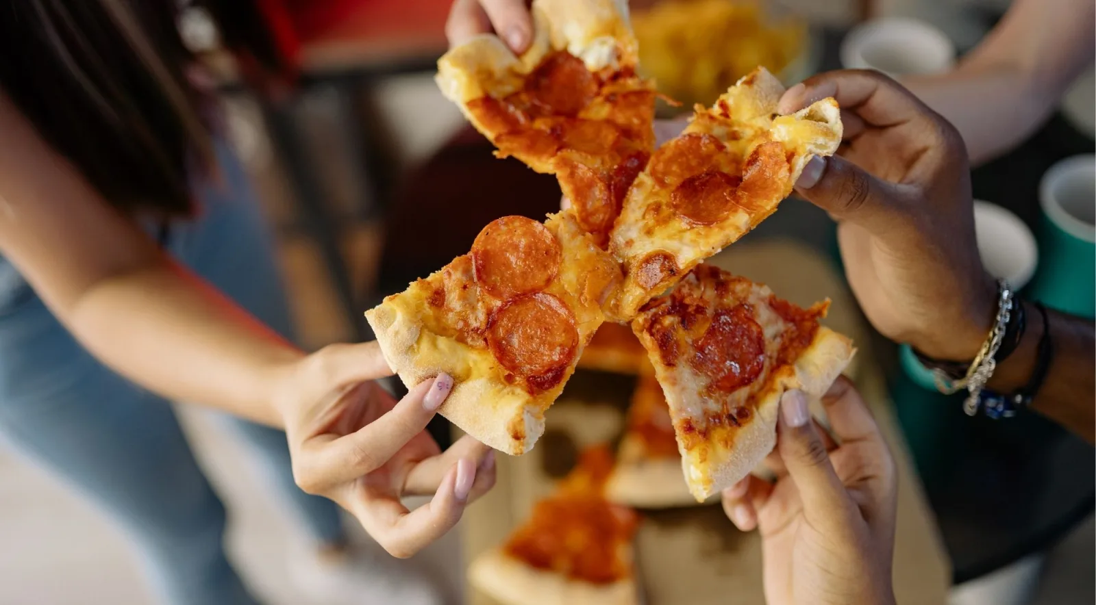 Four friends toasting with freshly baked pizza slices, holding them together in celebration after a Naples pizza class