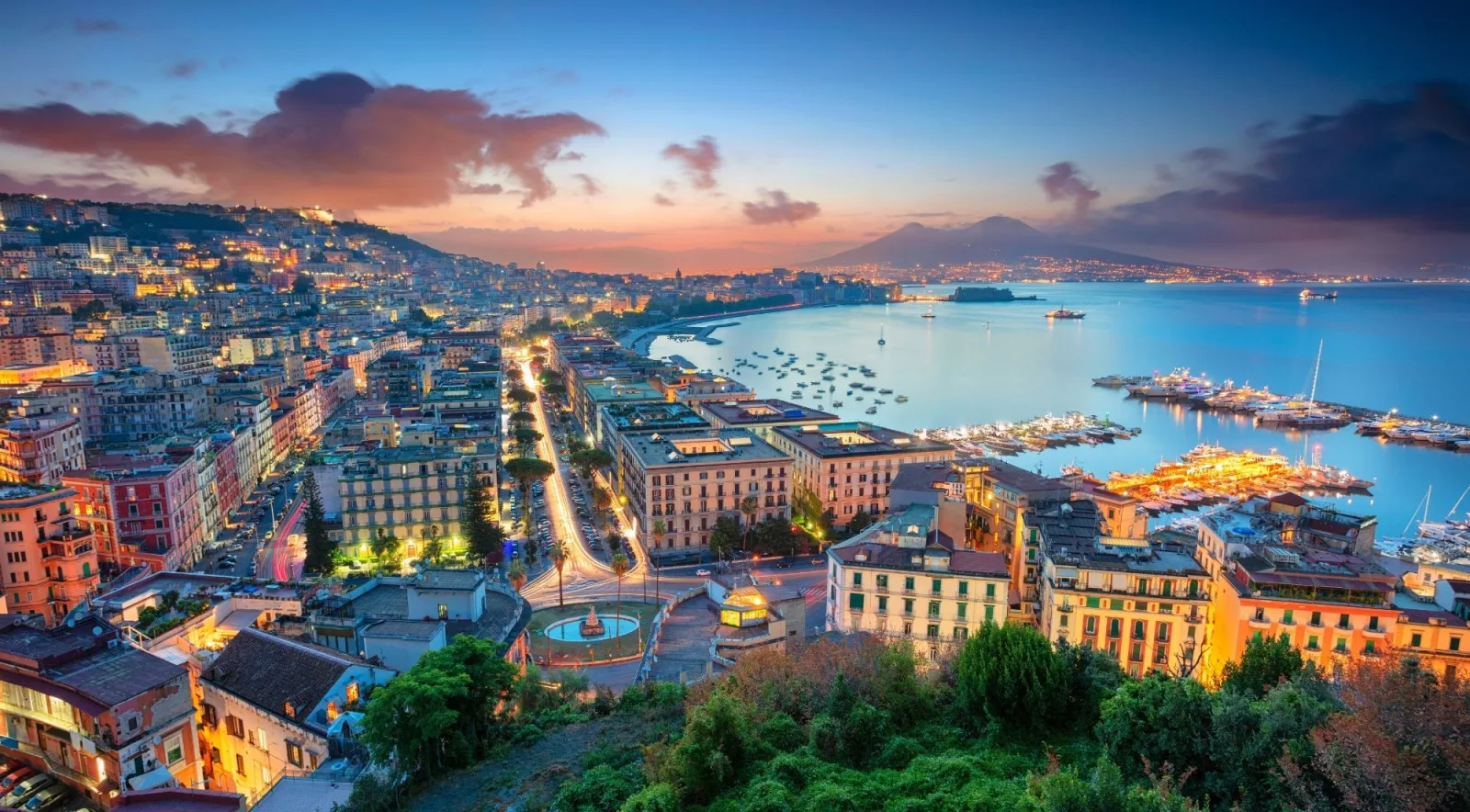 Panoramic view of Naples at sunset with the illuminated bay, city lights and Mount Vesuvius silhouetted in the background
